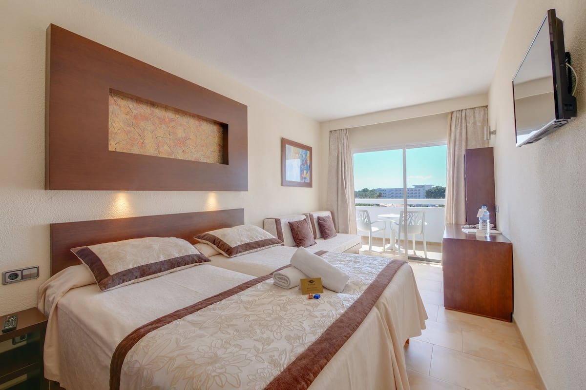 A hotel room with two beds, a desk, a TV, and a balcony with a view.