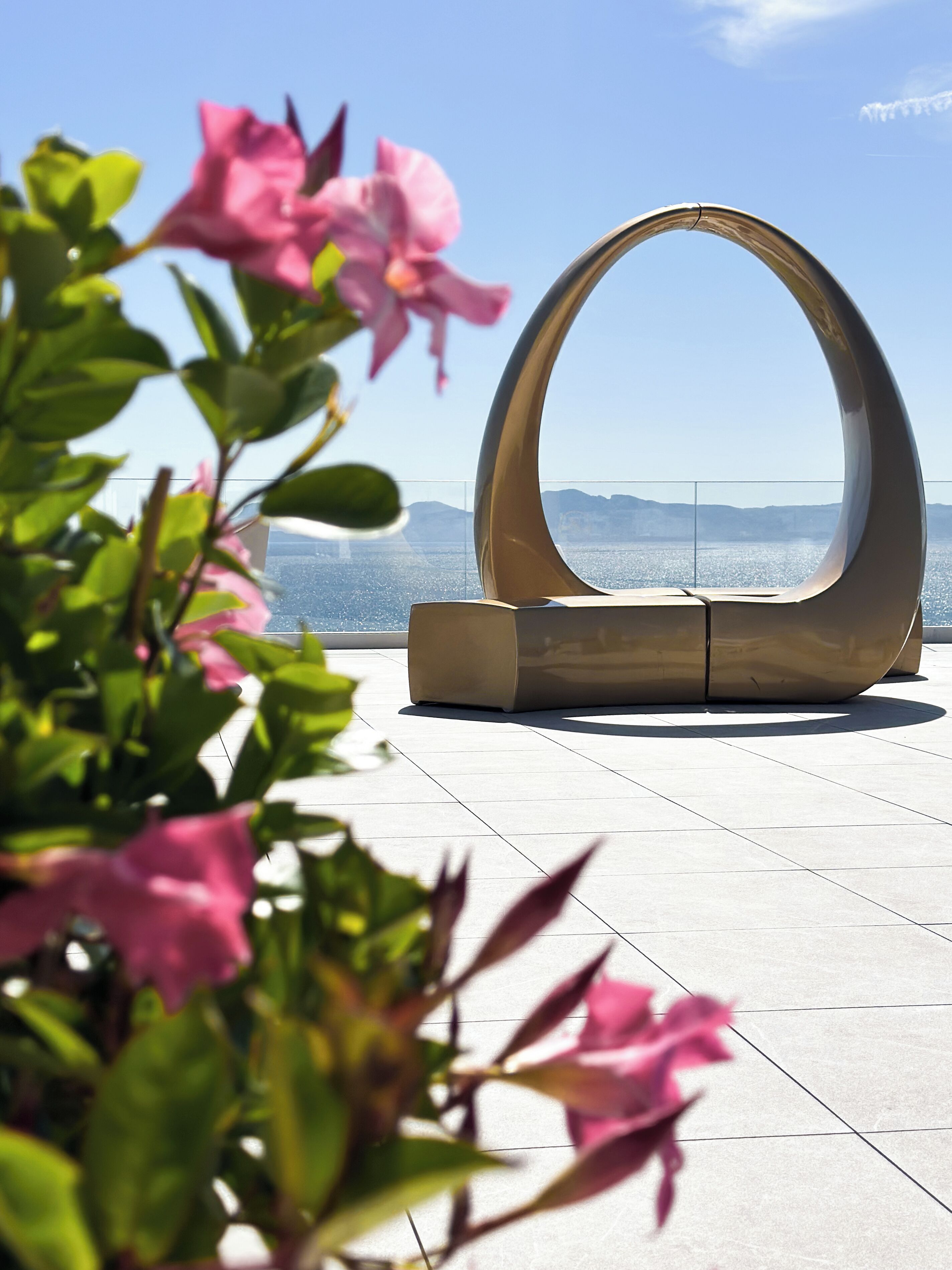 A modern outdoor seating area with a metallic structure and a view of the sea.