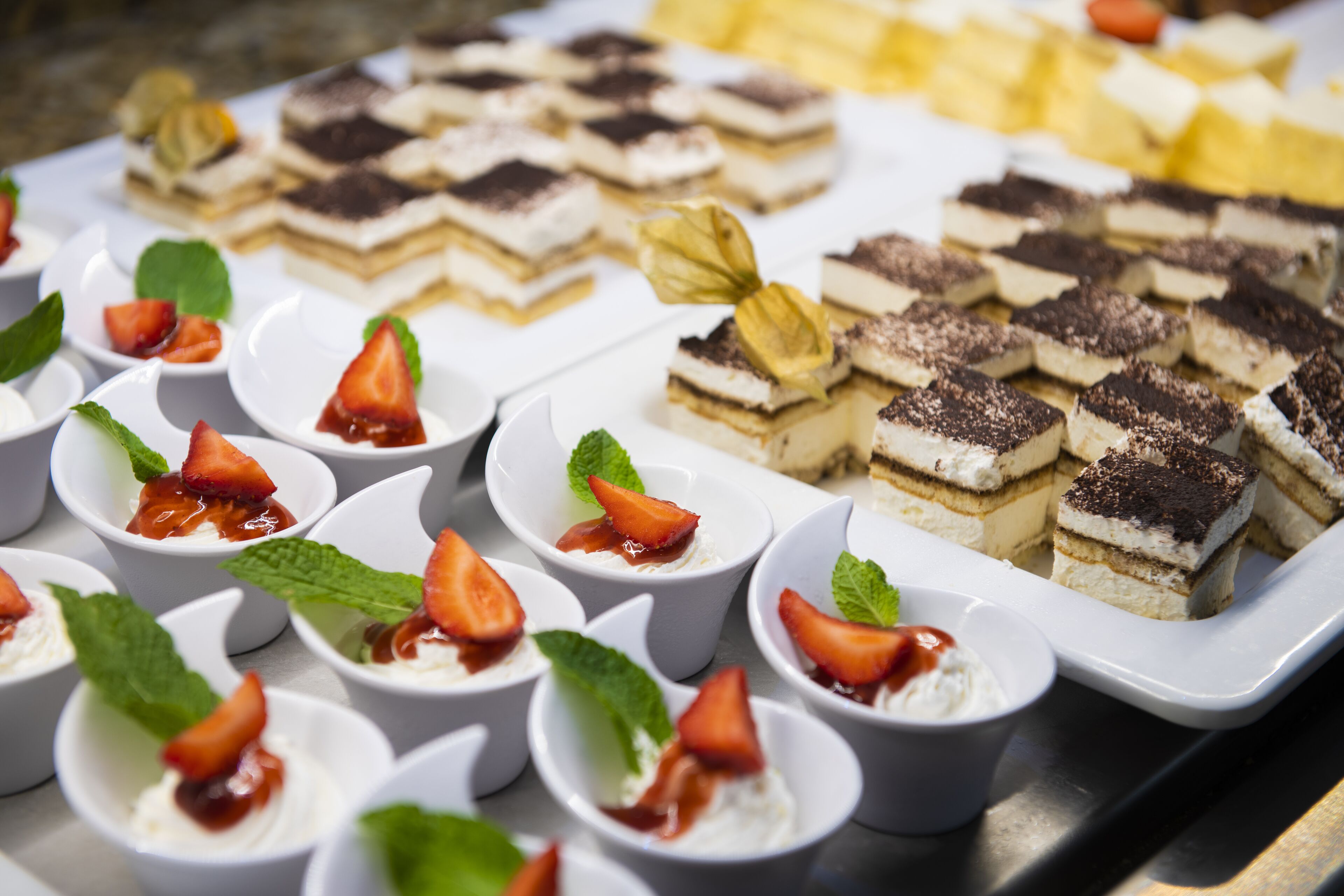 A variety of desserts arranged on a tray, including layered cakes and small bowls with whipped cream and strawberries.