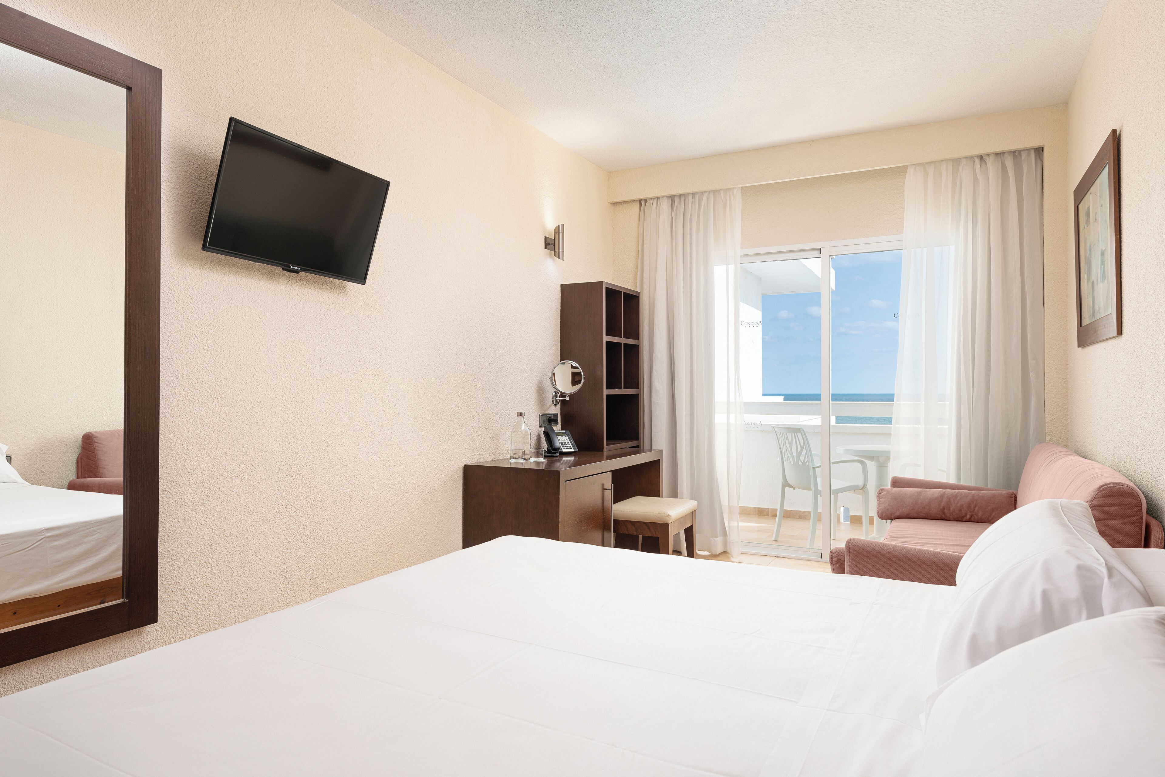 A hotel room with a bed, a desk with a chair, a television, and a window with curtains.