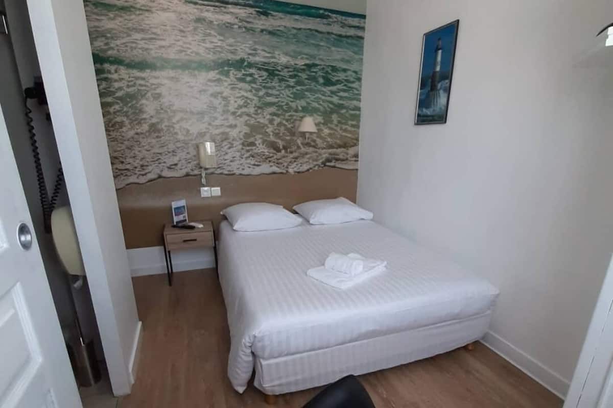 Ein Hotelzimmer mit Bett, Nachttisch, Lampe, einem Strandbild und einem Sessel.