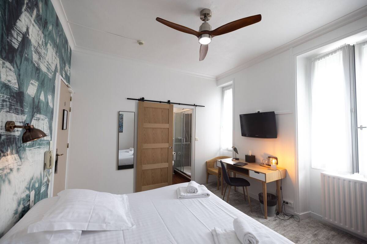 Ein Hotelzimmer mit Bett, Schreibtisch, Fernseher und Deckenventilator.
