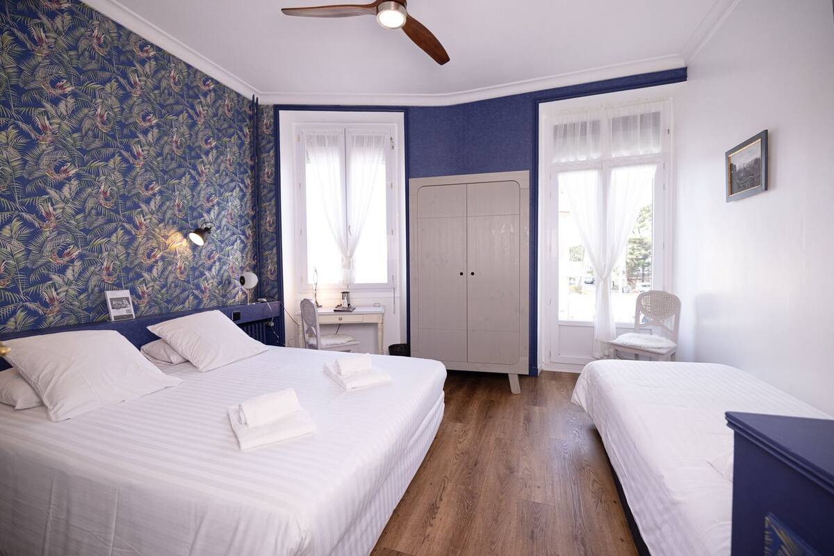 Ein Schlafzimmer mit zwei Betten, einem Schreibtisch, einem Kleiderschrank und einem Deckenventilator.
