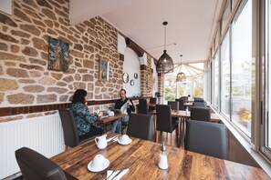Ein Restaurant mit Steinsäulen, Holztischen und schwarzen Stühlen.