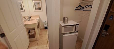 A compact bathroom with a sink, mirror, and a microwave.