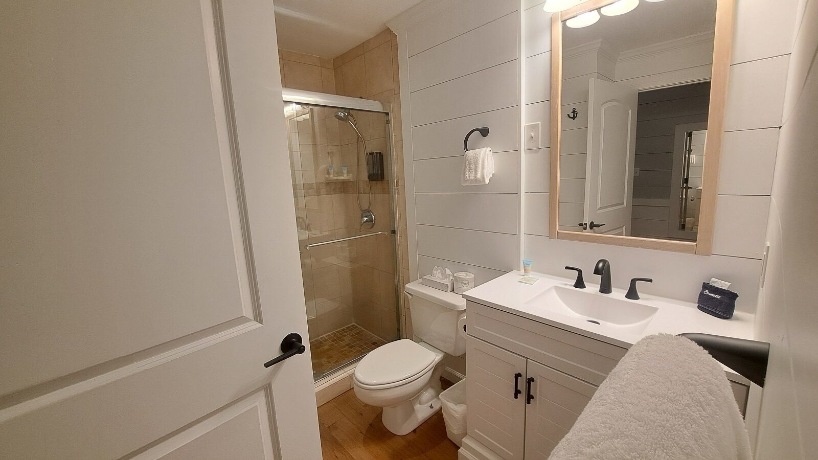 Ein Badezimmer mit einer gläsernen Duschkabine, einer weißen Toilette, einem Waschbecken mit Spiegel und einem Handtuchhalter.