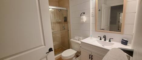 Ein Badezimmer mit einer gläsernen Duschkabine, einer weißen Toilette, einem Waschbecken mit Spiegel und einem Handtuchhalter.