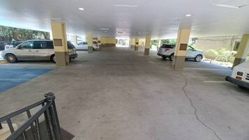 Area parcheggio coperta con diverse auto parcheggiate, pavimento in cemento e pilastri con segnaletica.