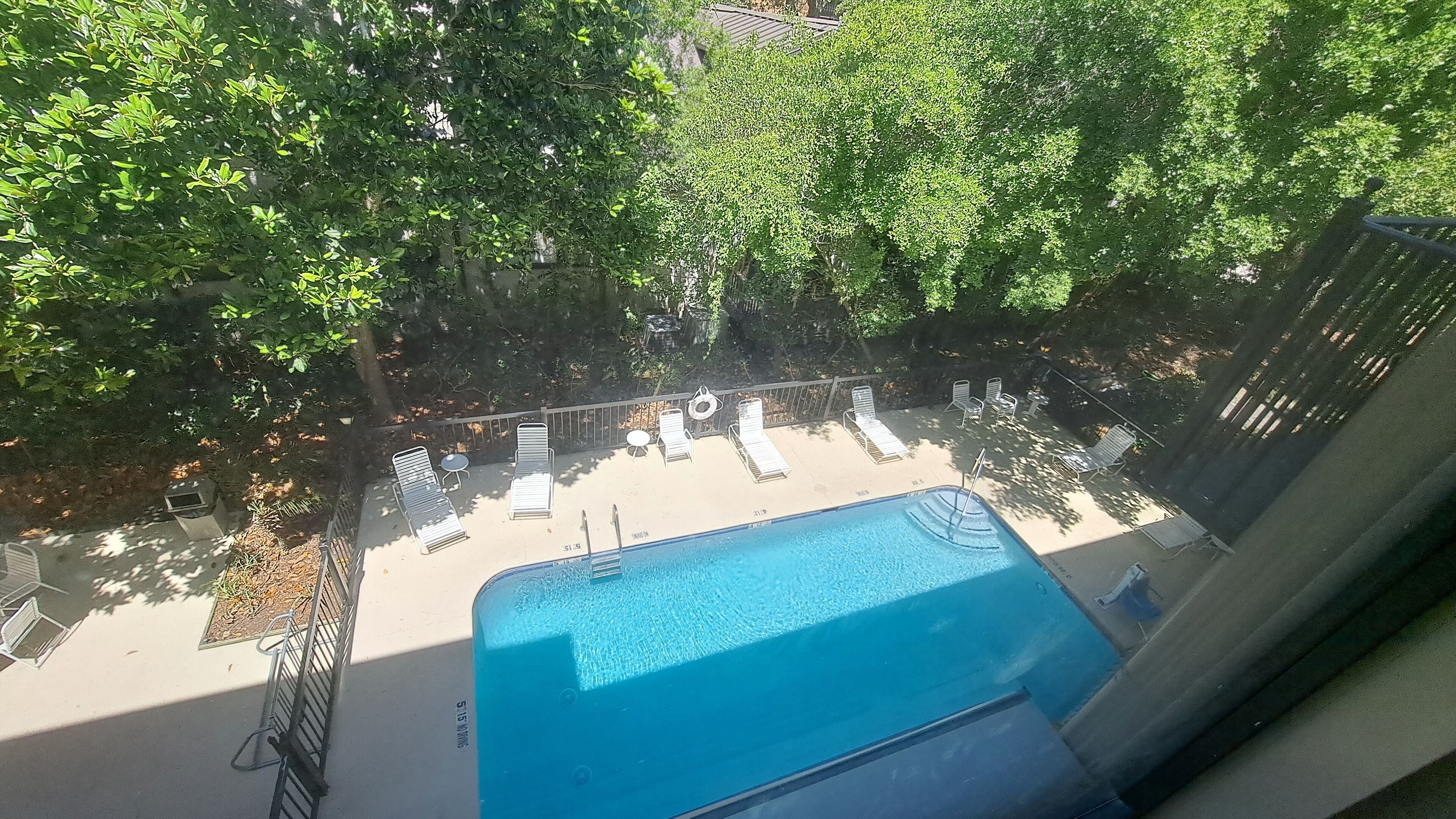 A pool area with lounge chairs and a small table, surrounded by trees.