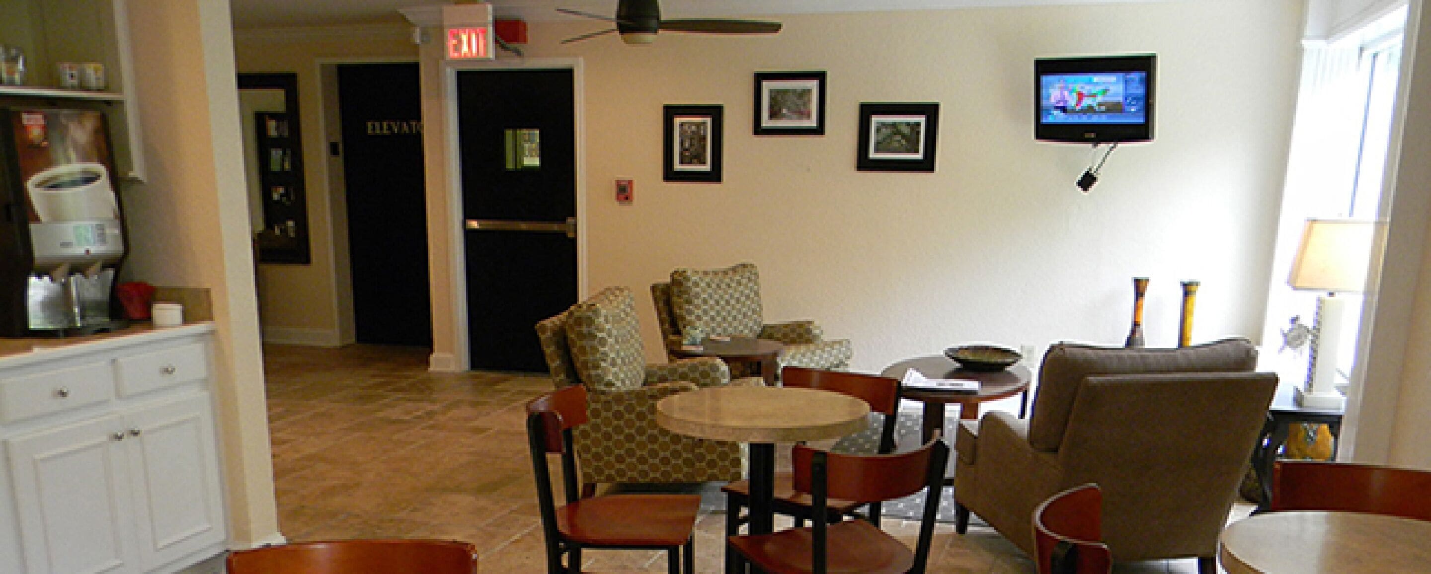 A living room with a TV, chairs, a table, and a coffee machine.