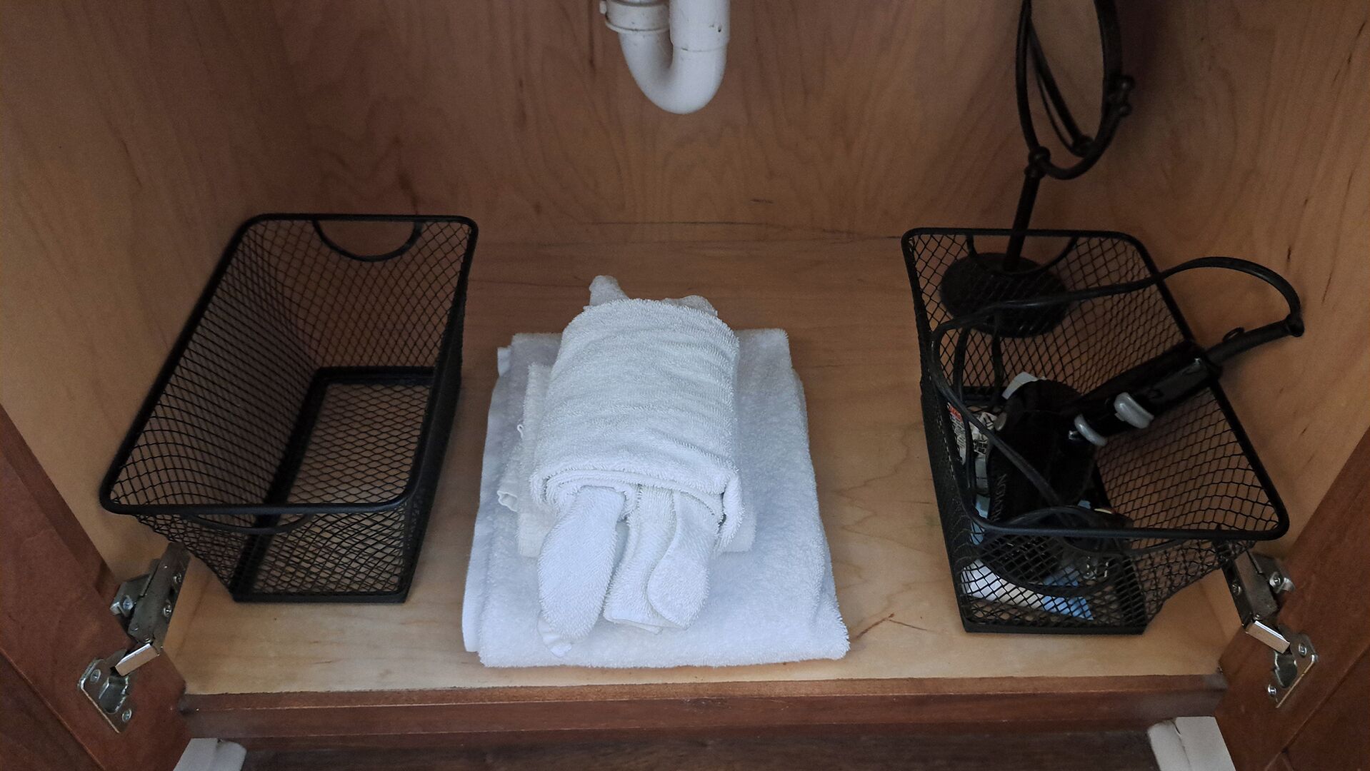A wooden cabinet with a white towel folded on top, two black mesh baskets, and a white pipe above.