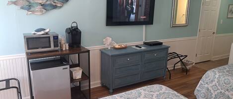 A compact hotel room with a kitchenette, a flat-screen TV, a dresser, and two beds with patterned bedding.