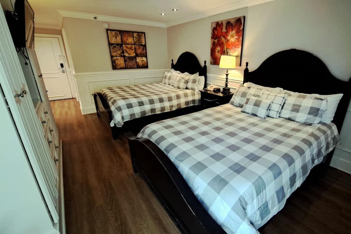 Hotellihuone, jossa on kaksi sänkyä, yöpöytä, lamppu, taulu ja rottinkituoli.