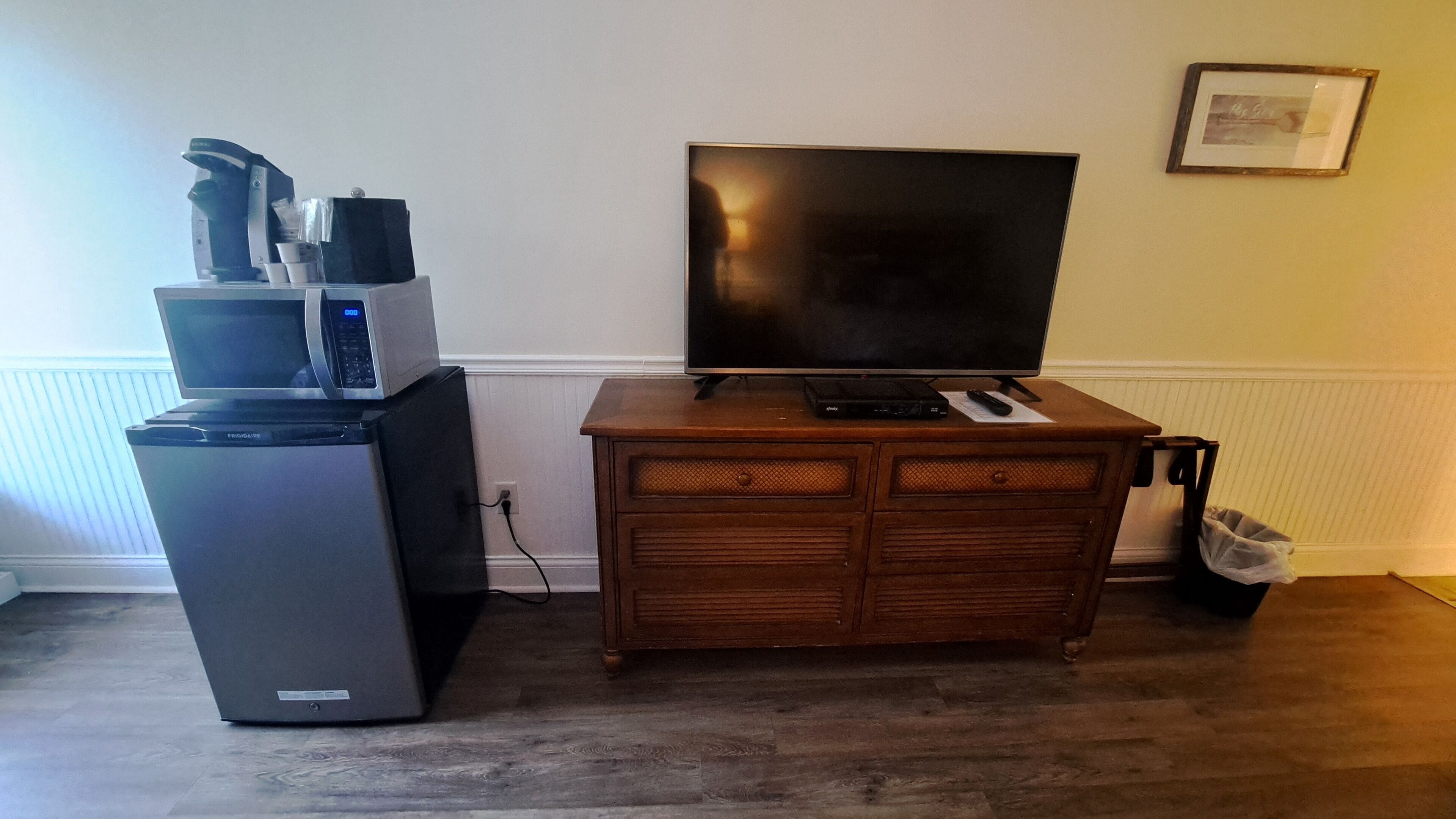 A living room with a flat-screen TV, a coffee maker, and a refrigerator.