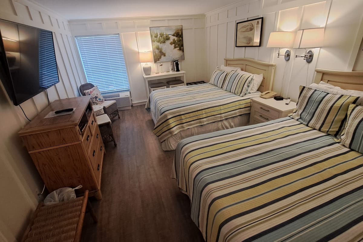 Hotellihuone, jossa on kaksi sänkyä, työpöytä, tuoli, televisio ja ikkuna, jossa on sälekaihtimet.
