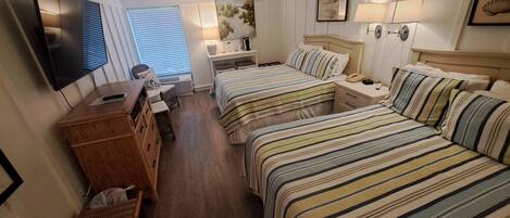 A hotel room with two beds, a desk, a chair, a TV, and a window with blinds.