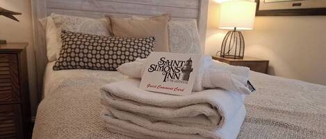 A neatly made bed with a guest comment card, a patterned pillow, and a lamp on a bedside table.