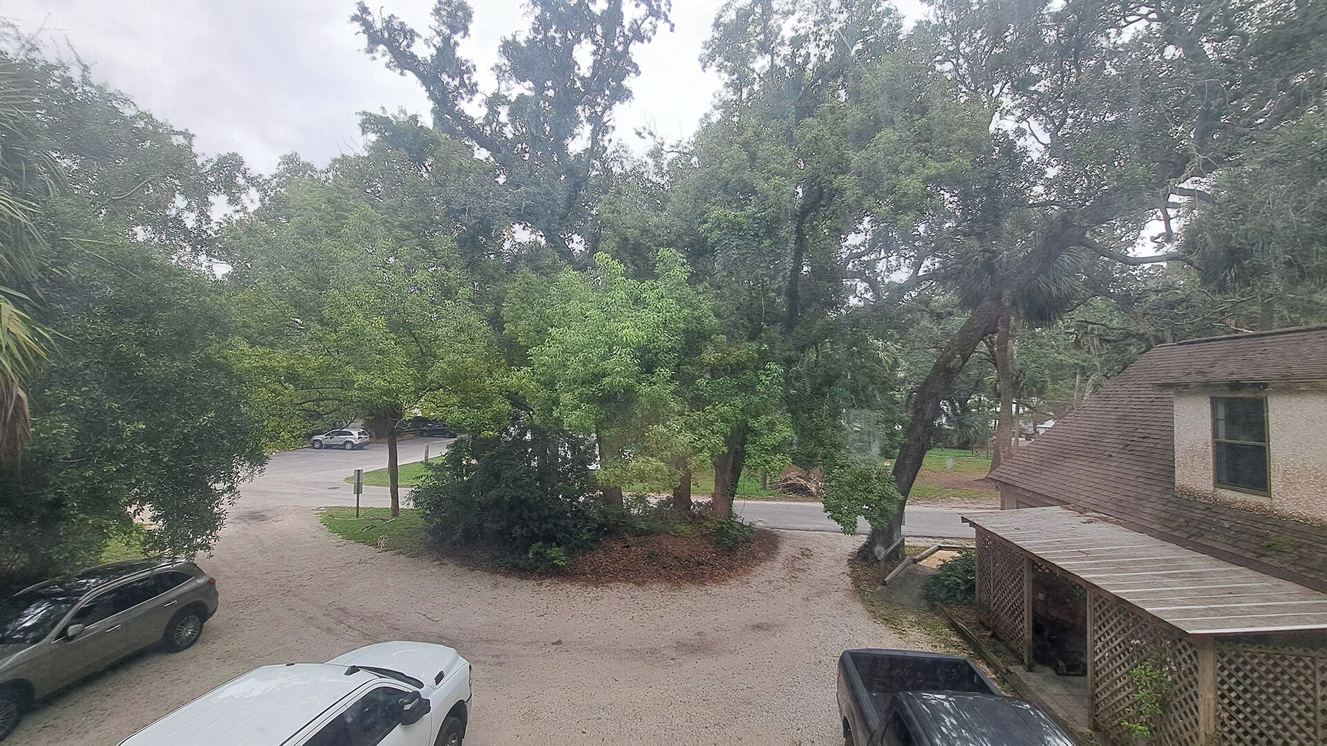 A parking area with a gravel path, a white car, and a building with a wooden deck.
