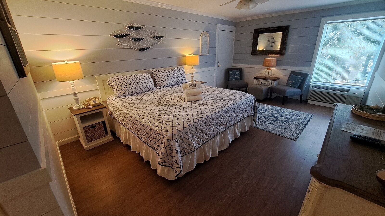 A bedroom with a bed, bedside lamps, a nightstand, a rug, and a window with blinds.