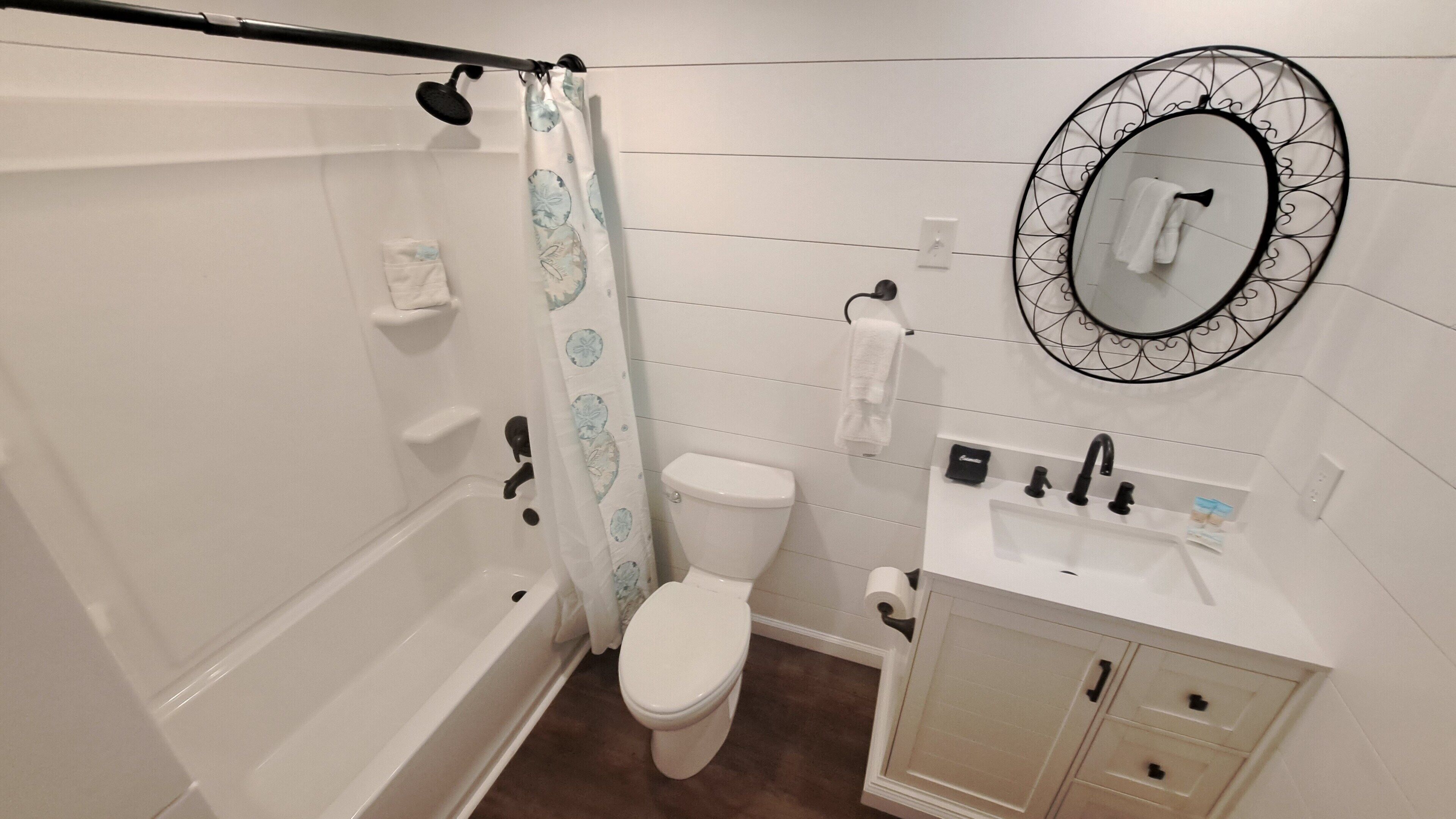 A bathroom with a bathtub, toilet, sink, and a mirror with a decorative frame.