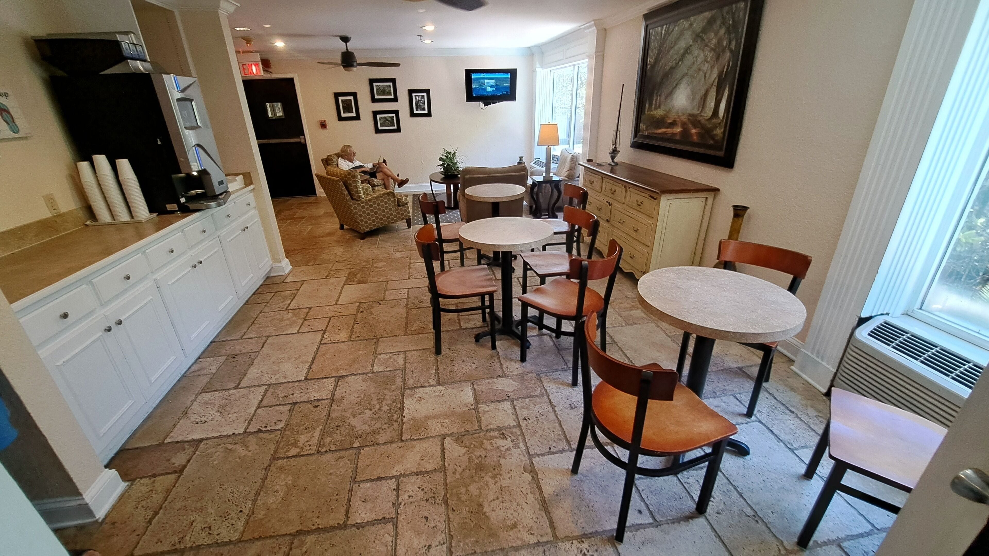 A spacious kitchen with a dining area, a television mounted on the wall, and a large window providing natural light.