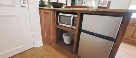 A compact kitchen with a microwave, refrigerator, and wooden cabinets.