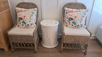 Two wicker chairs with matching cushions, a small woven stool, and a wooden cabinet in a room with a wooden floor.