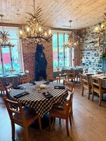 A restaurant with checkered tablecloths, wooden chairs, and antler chandeliers.