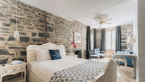 Ein Schlafzimmer mit Steinwand, einem Bett mit gemustertem Überwurf, einem Schreibtisch und einem Stuhl.