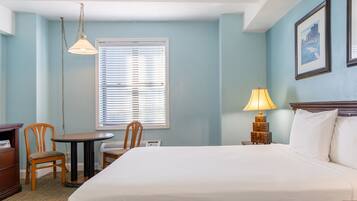 Habitación de hotel con cama, escritorio, dos sillas, lámpara y ventana con persianas.