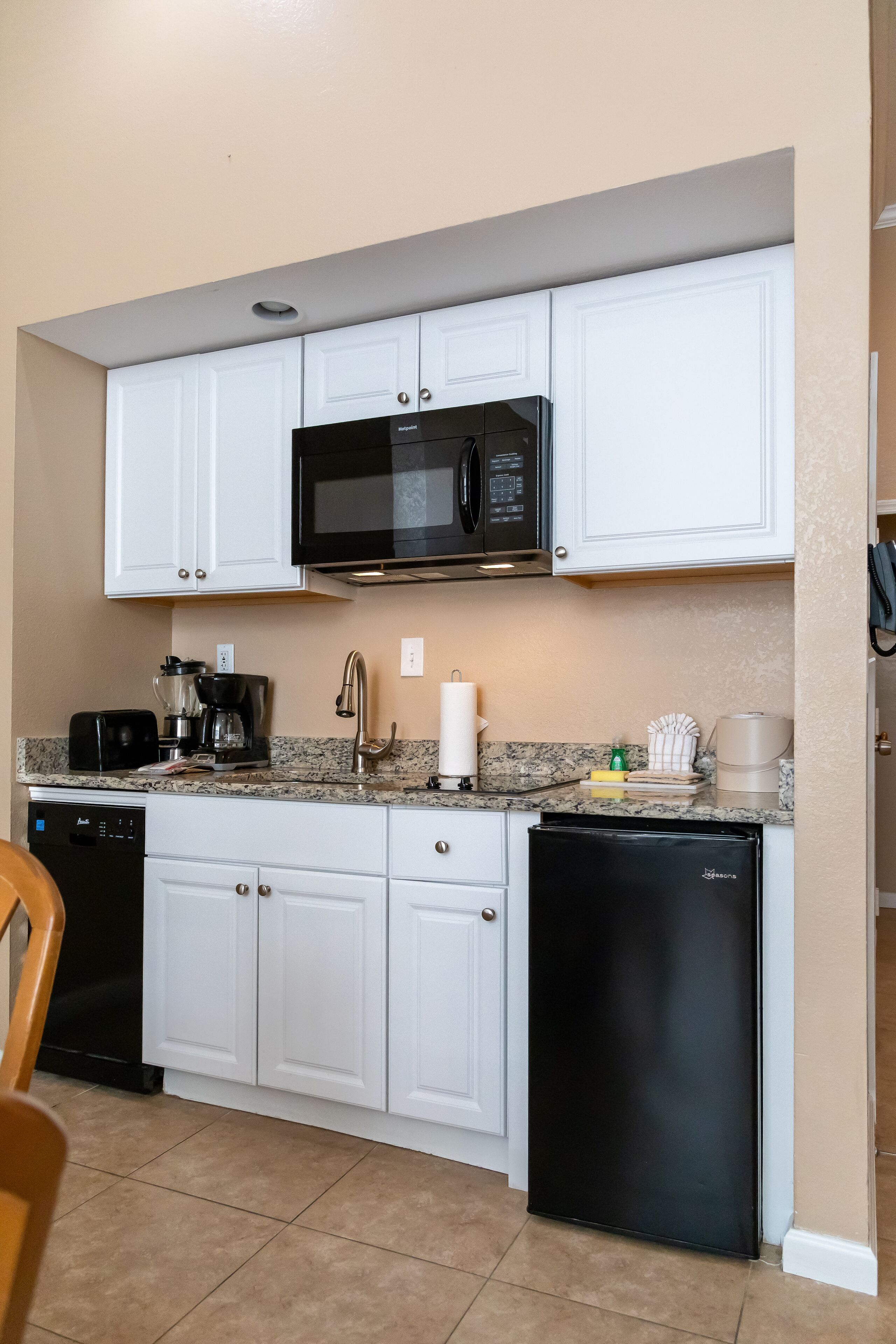 A compact kitchen with white cabinets, a black microwave, a coffee maker, and a dishwasher.