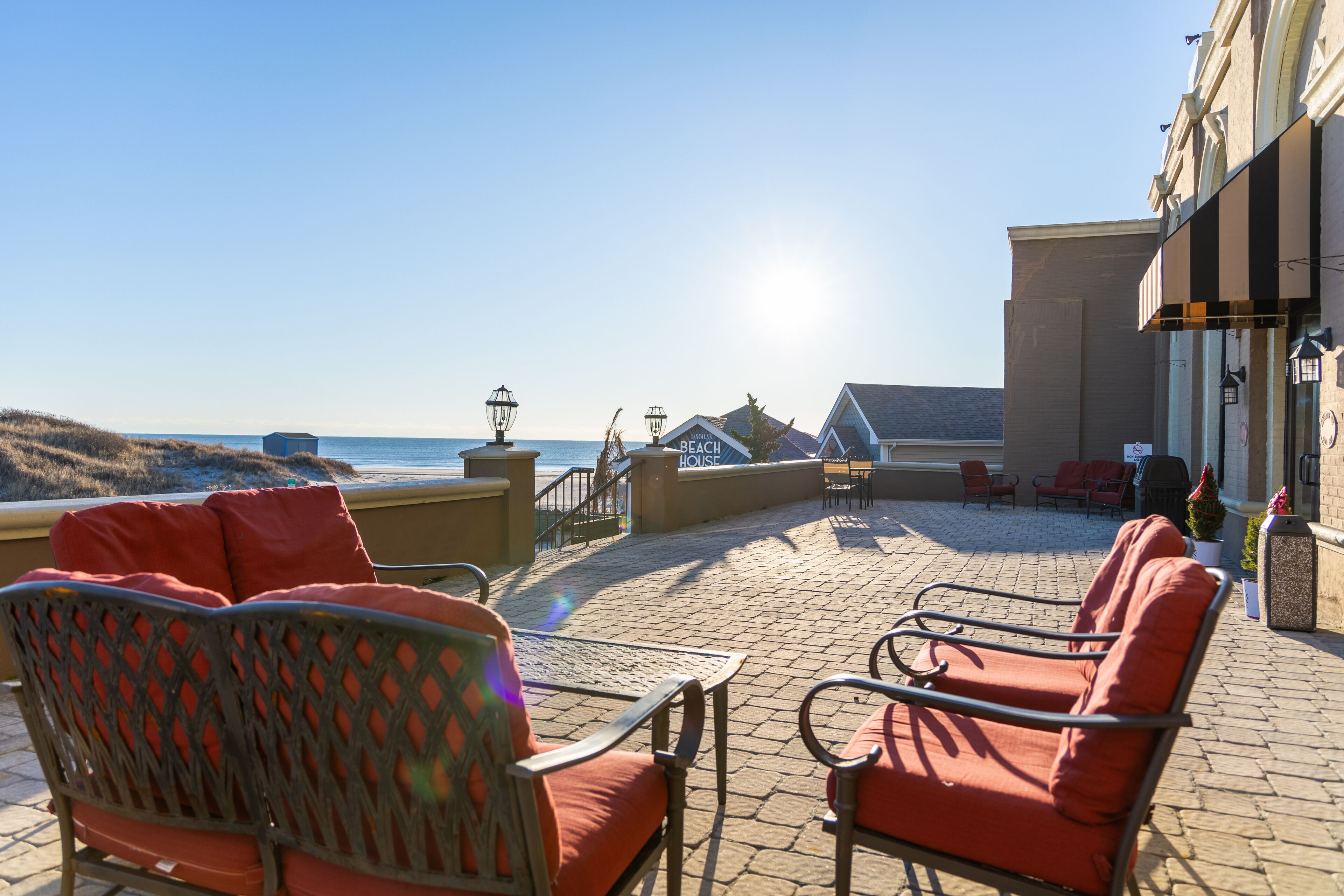 An outdoor seating area with wicker chairs and a table, overlooking the beach and ocean.