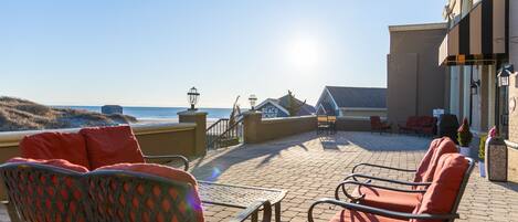 An outdoor seating area with wicker chairs and a table, overlooking the beach and ocean.