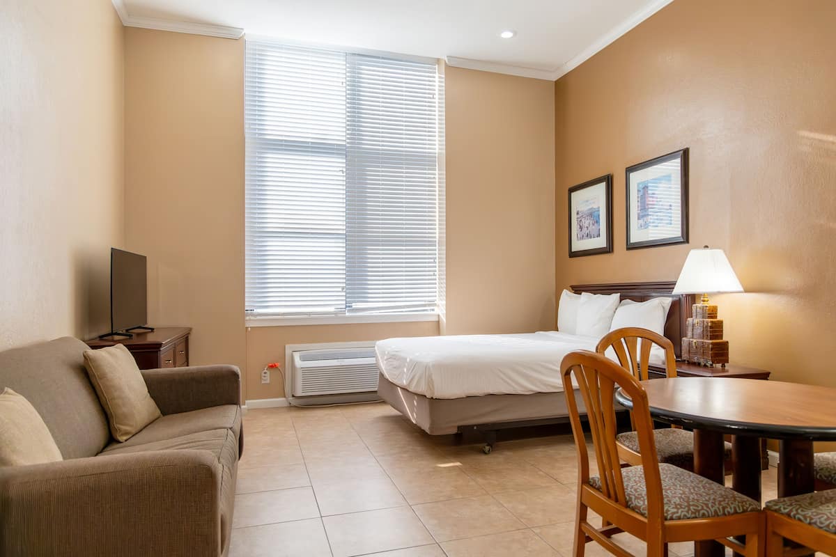 A hotel room with a bed, a sofa, a dining table, and a TV.