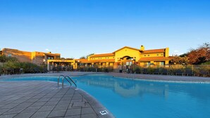 A swimming pool with a tiled deck, a building with a yellow facade, and a clear blue sky. - WorldMark Rancho Vistoso (Oro Valley)