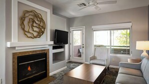 A living room with a fireplace, a television, a ceiling fan, and a large window. - WorldMark Rancho Vistoso (Oro Valley)