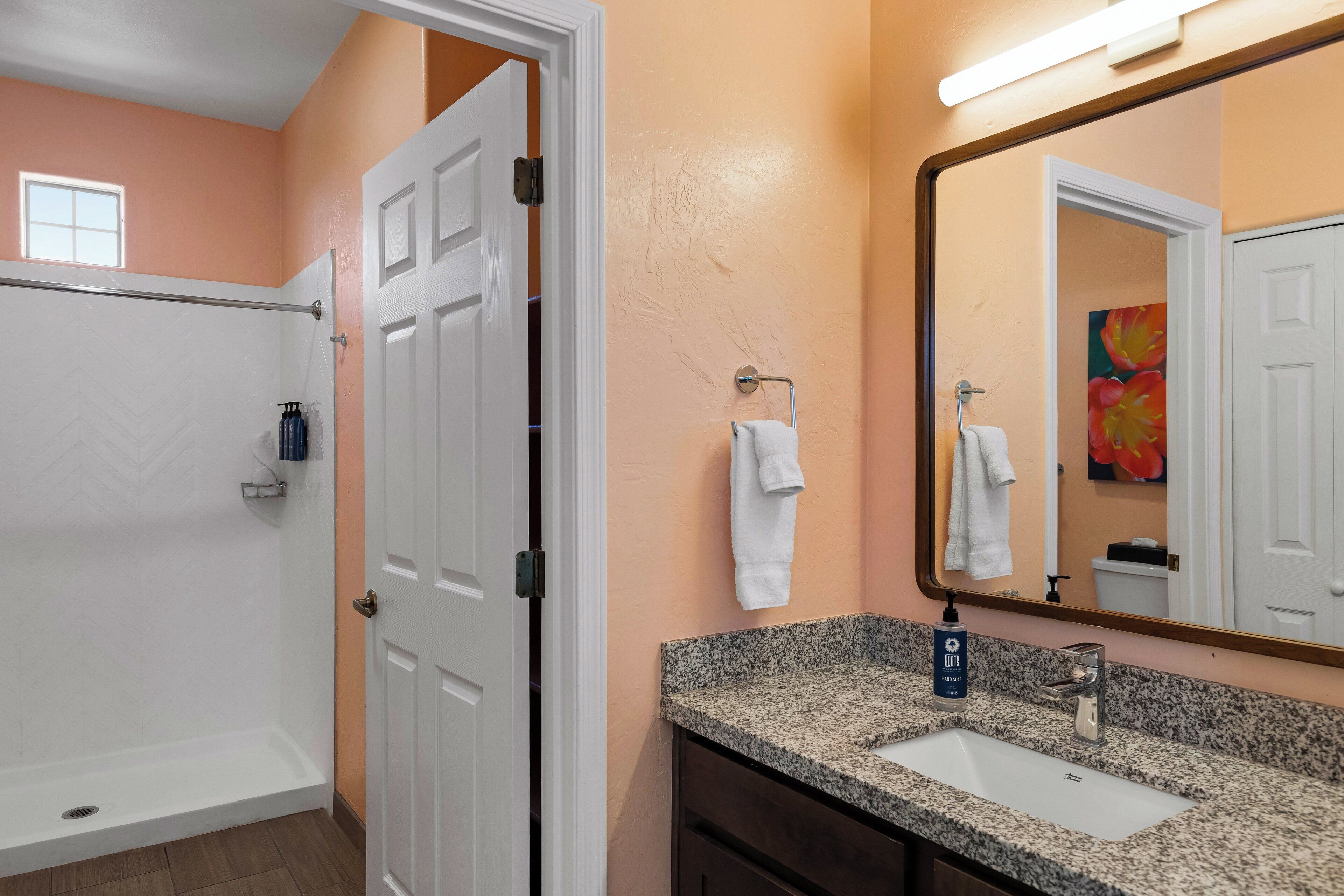 A bathroom with a shower, sink, and a large mirror.