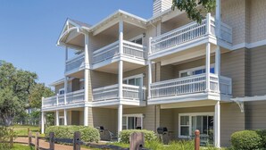 A multi-story building with balconies, a paved walkway, and a landscaped area with mulch and plants.