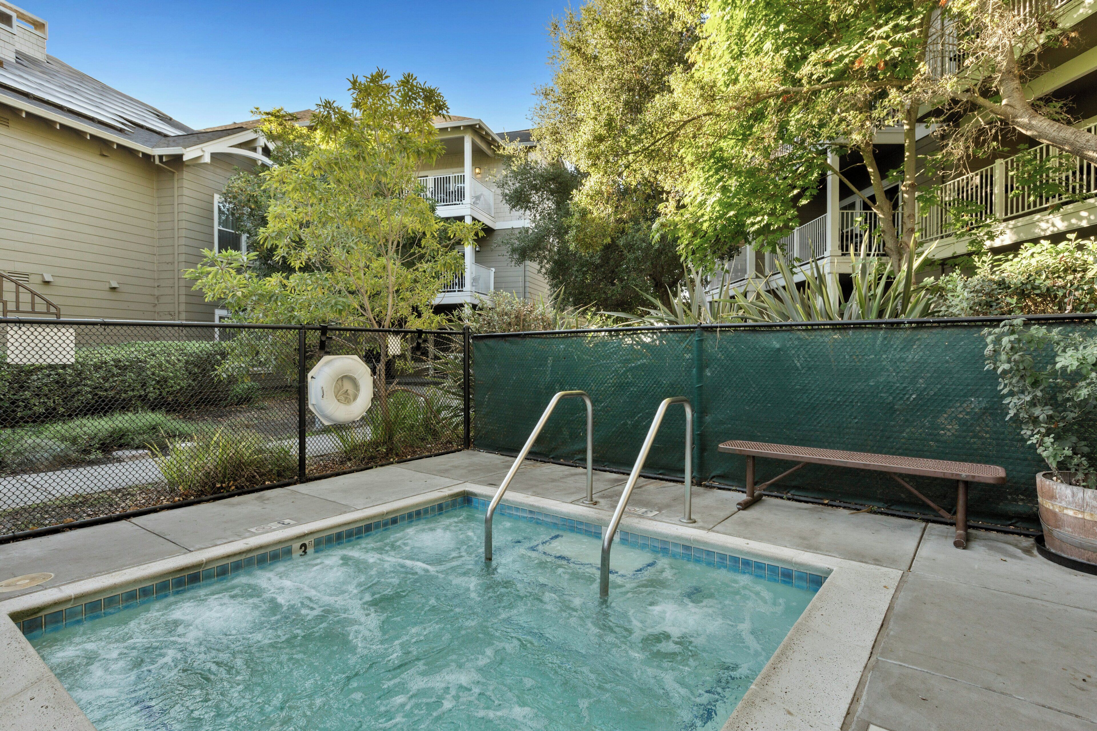 A swimming pool with a metal ladder, surrounded by a fence and greenery.