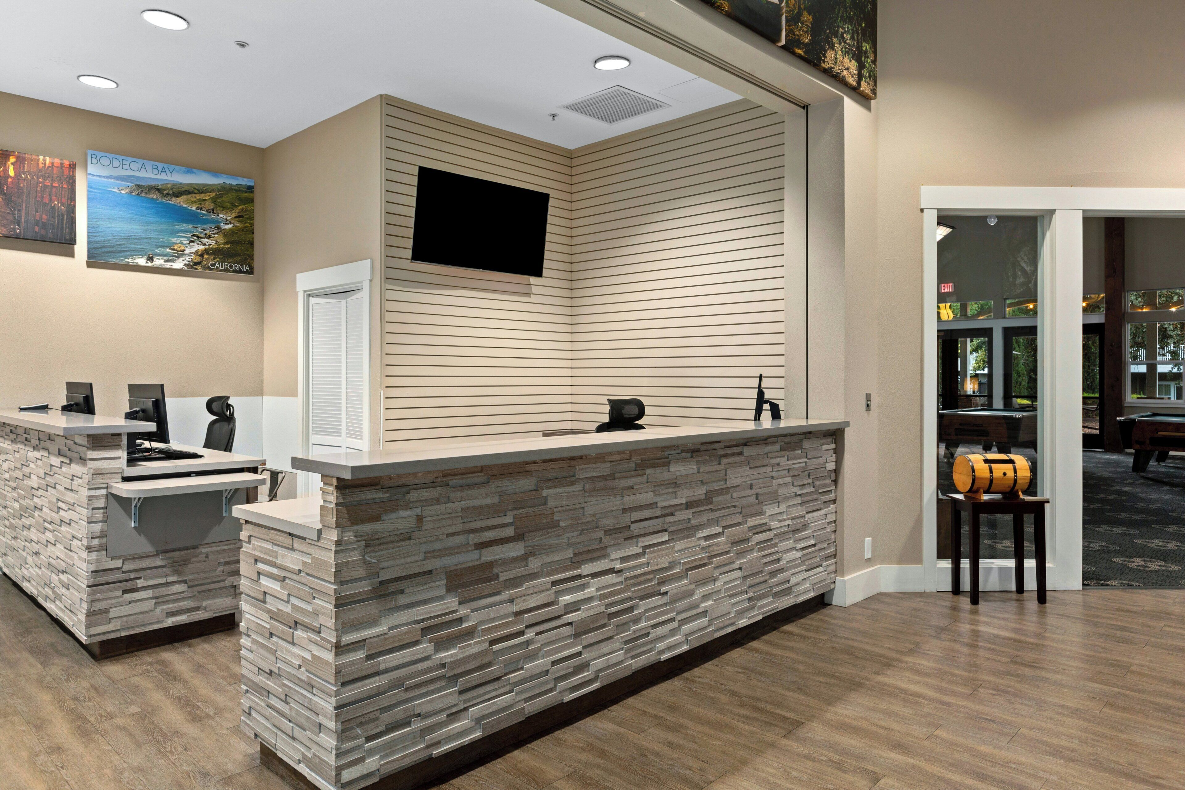 A reception desk with a stone facade, a mounted flat-screen TV, and a door leading to a pool area.