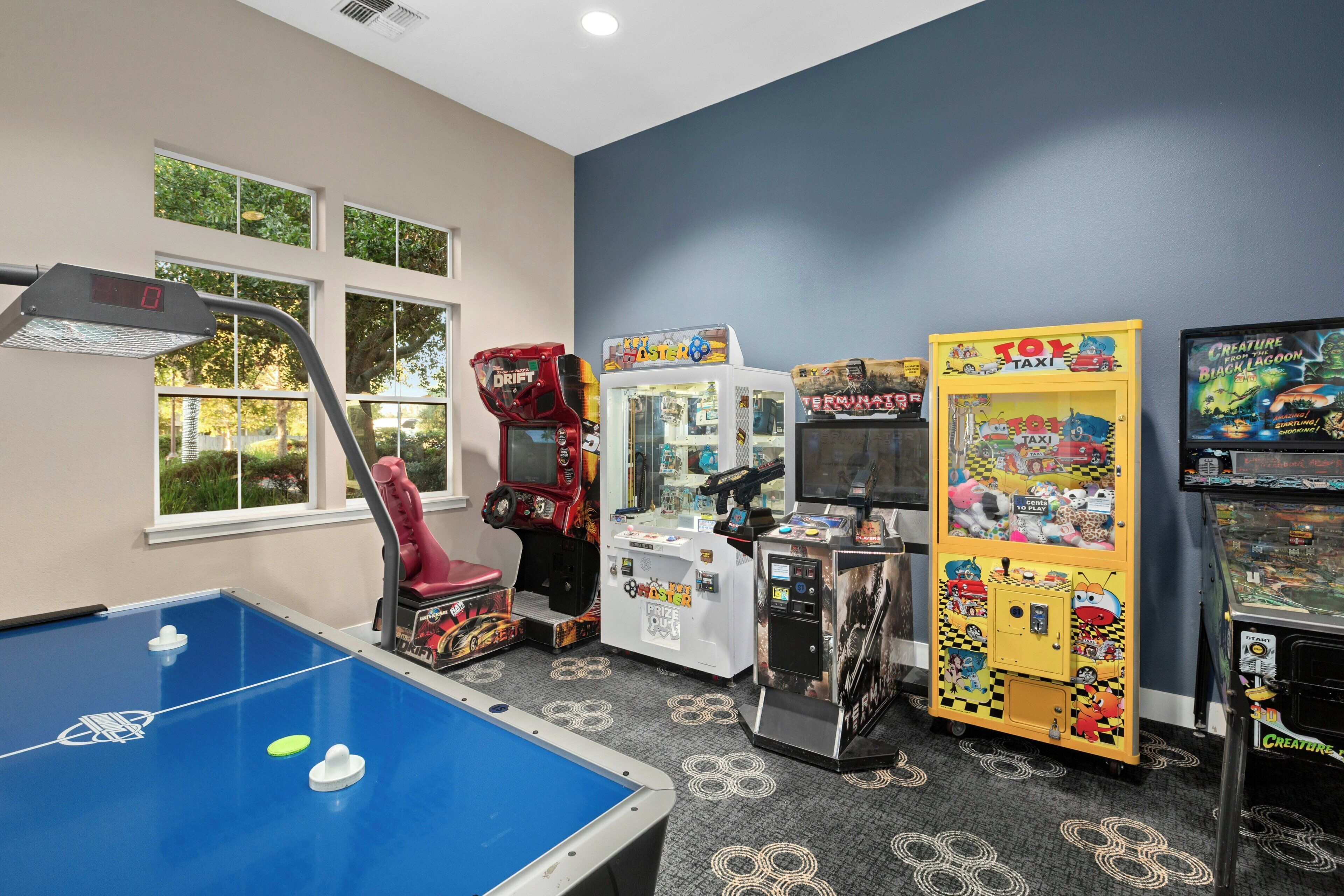 A room with a pool table, arcade games, and a window with a view of greenery.