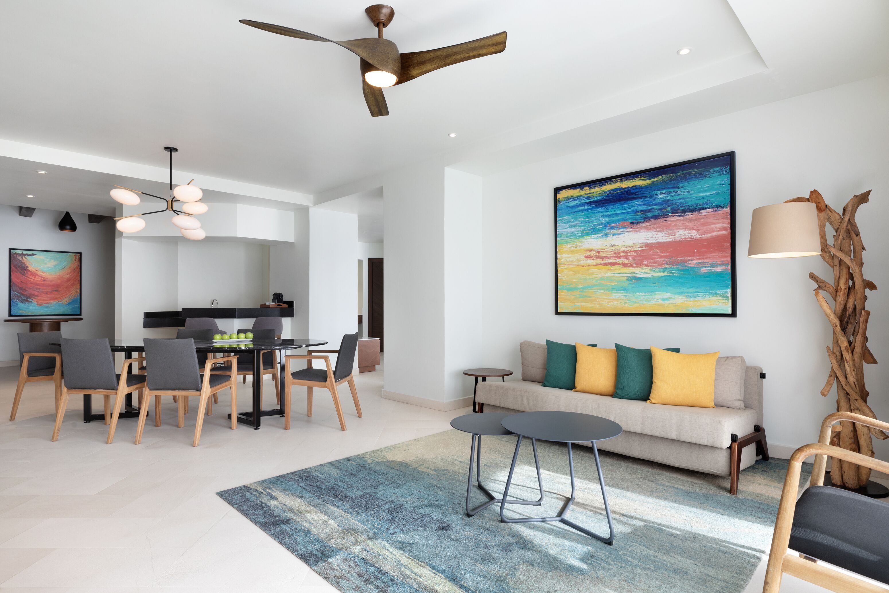 A modern living room with a dining area, a ceiling fan, a large abstract painting, and a wooden sculpture.