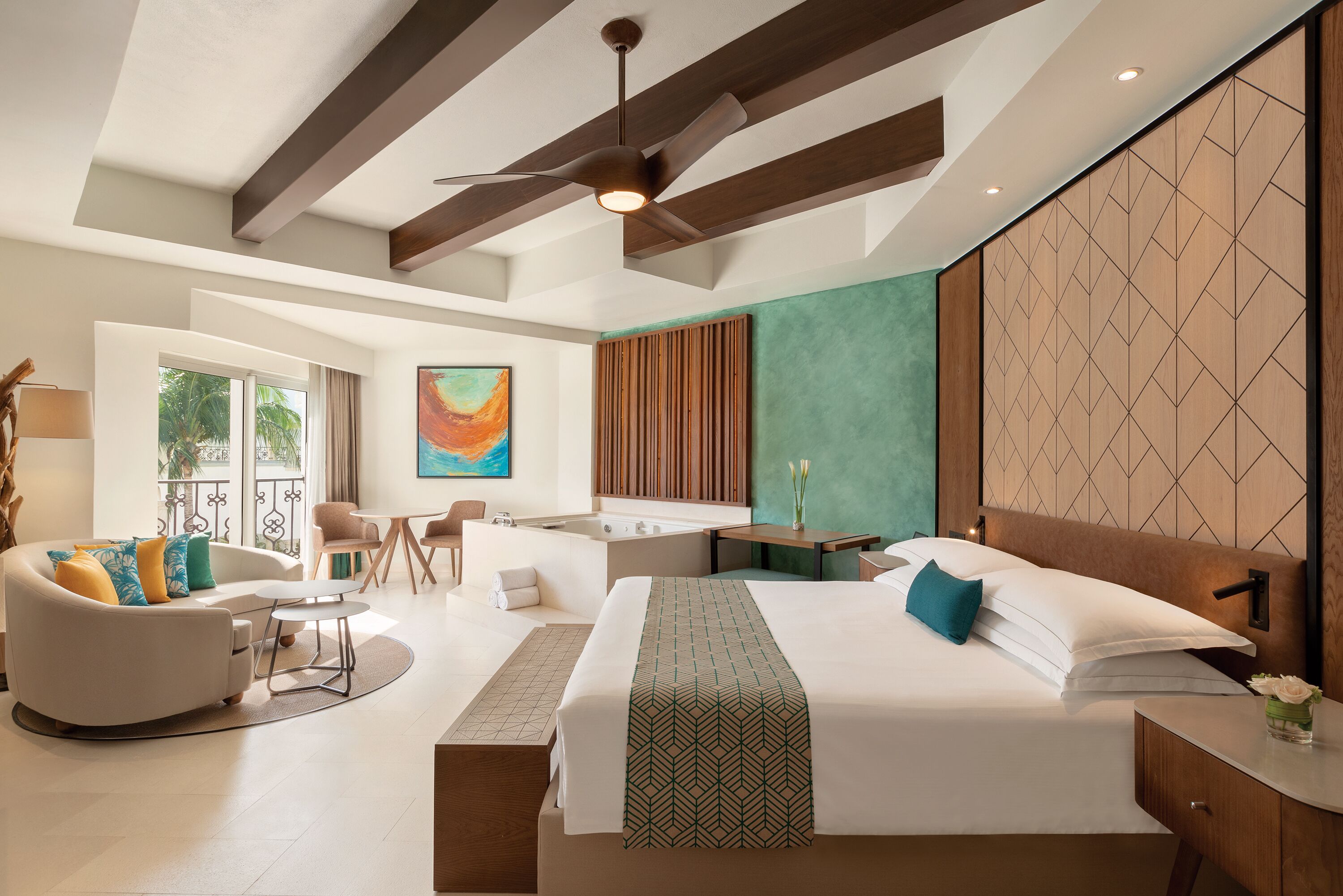 Una habitación de hotel moderna con una cama grande, un escritorio, un sofá y un balcón con vistas a palmeras.
