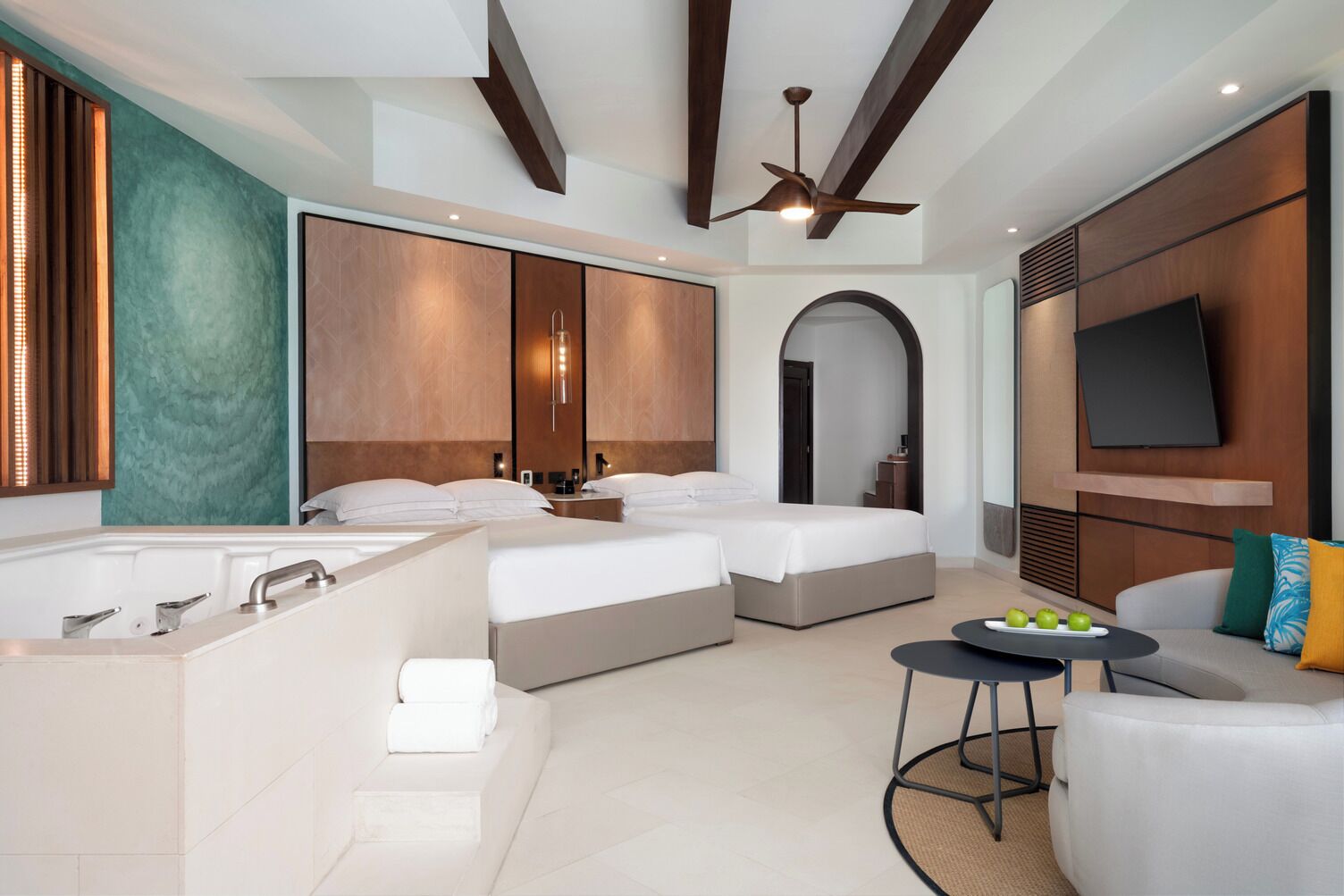 A modern hotel room with a large bed, a separate bedroom, a sitting area with a TV, and a bathtub.