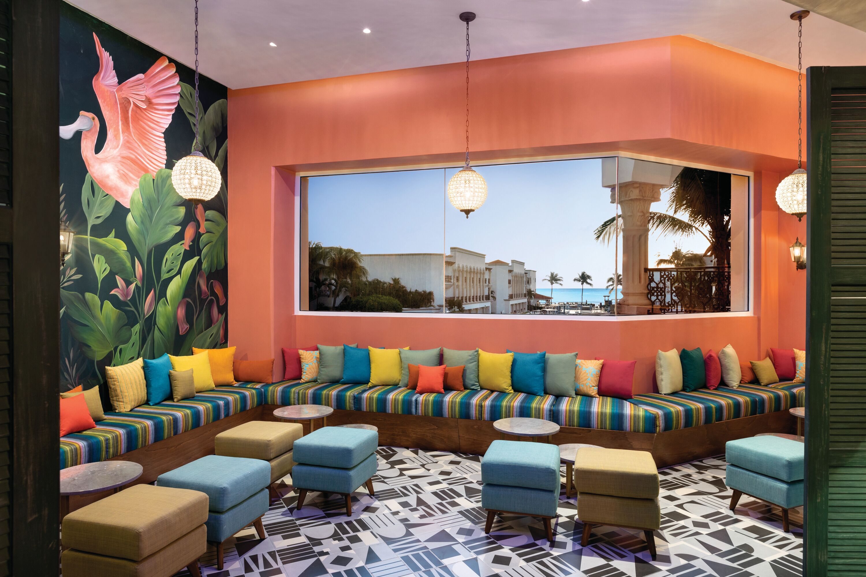 A vibrant room with a large window, colorful seating, and a tropical mural.