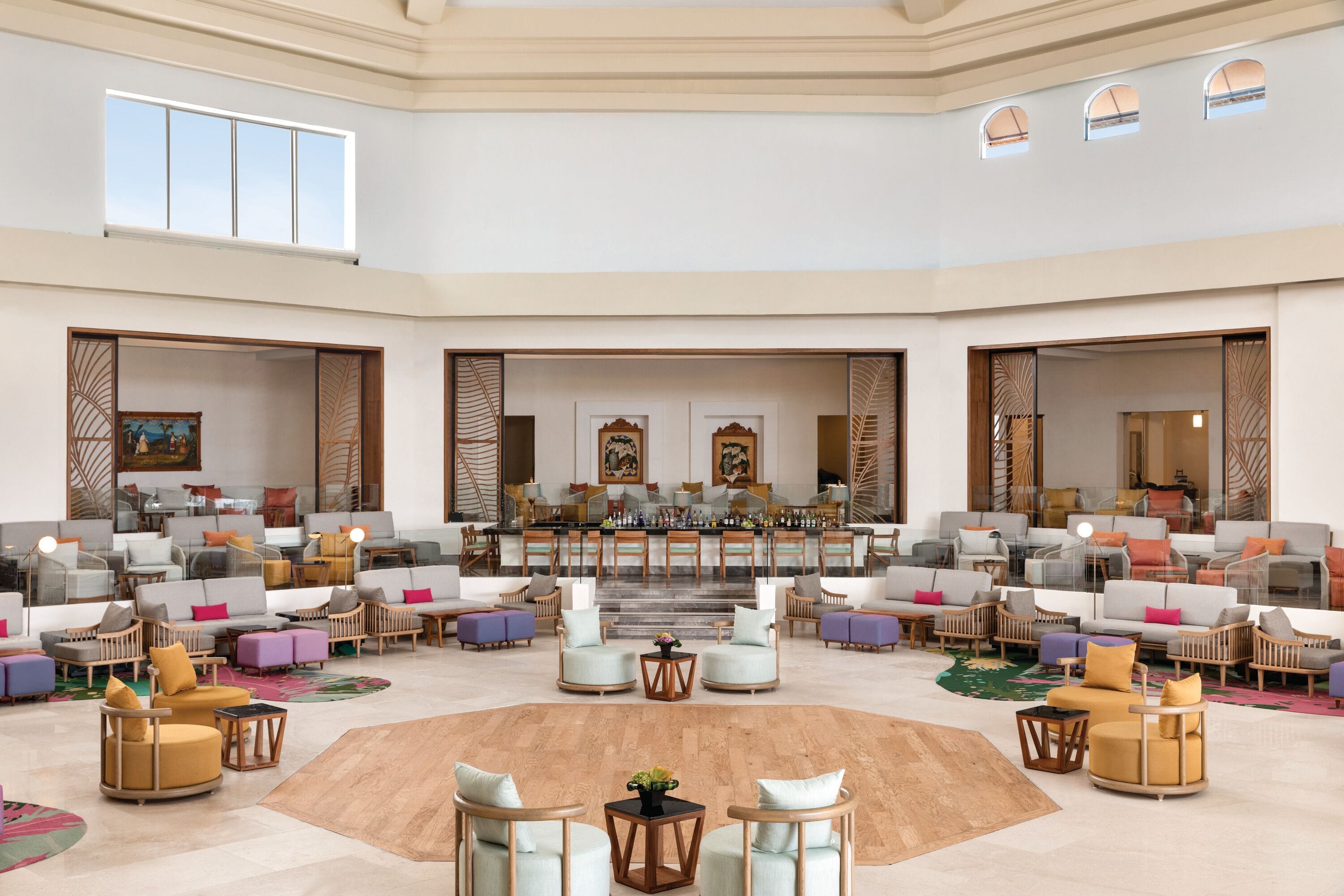Eine geräumige Lobby mit mehreren Sitzbereichen, einer zentralen Bar und einer Treppe zu einer oberen Ebene.