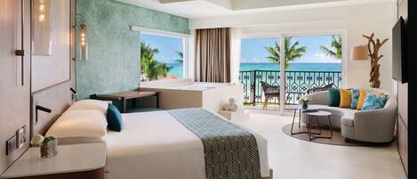 A modern hotel room with a large bed, a desk, a balcony with a view of the ocean, and a ceiling fan.