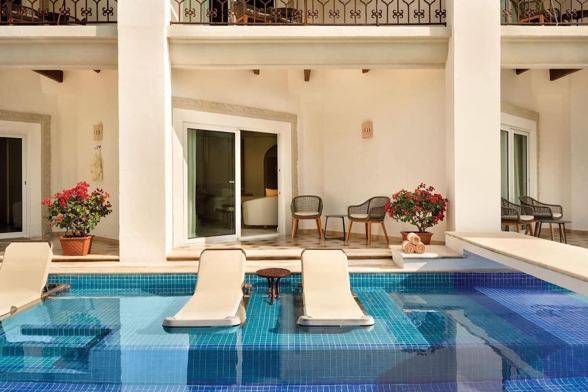 Zona de piscina con sillones reclinables, plantas en macetas y vistas al interior.