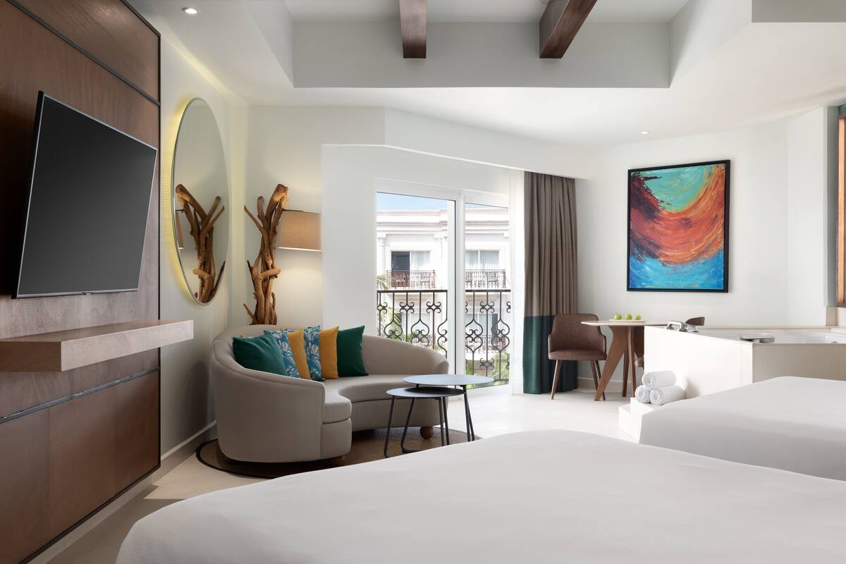 Una habitación de hotel moderna con una cama grande, un sofá, una mesita, un televisor y un balcón con vistas.