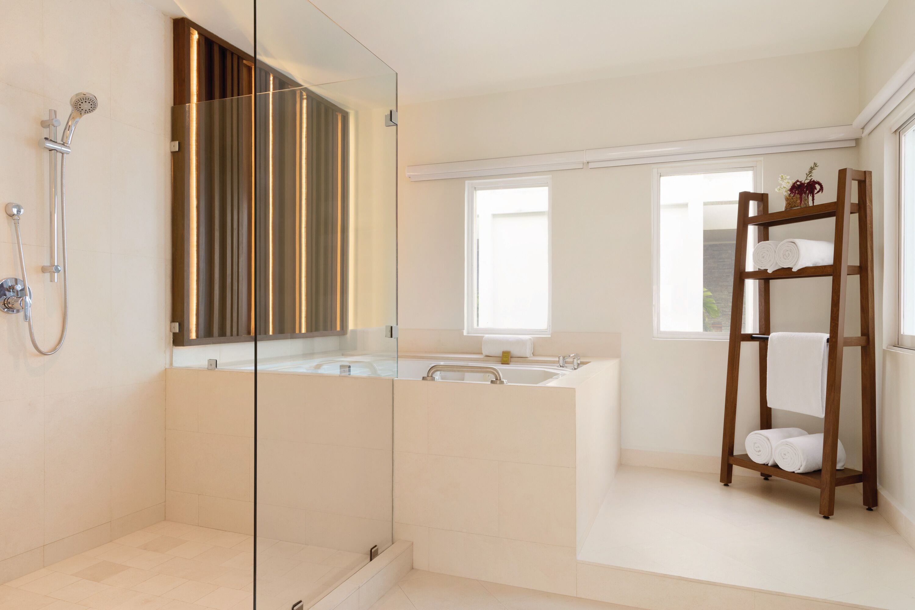 A modern bathroom with a glass-enclosed shower, a large bathtub, and a wooden towel rack.